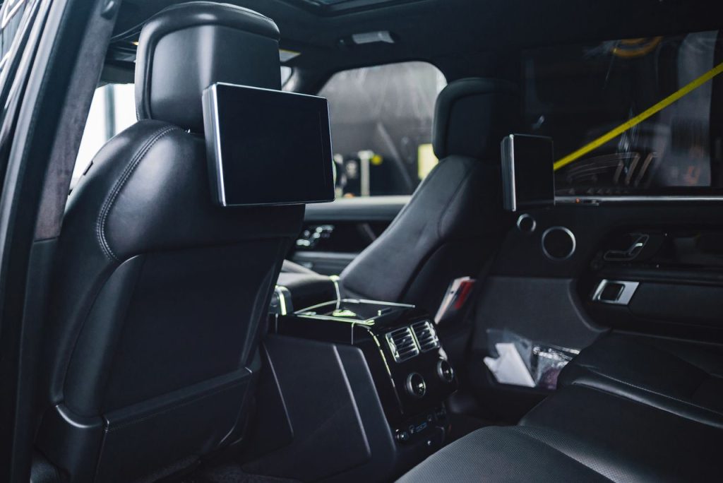 Contemporary style auto interior with rectangular displays on back seats and entertainment equipment with buttons in daylight