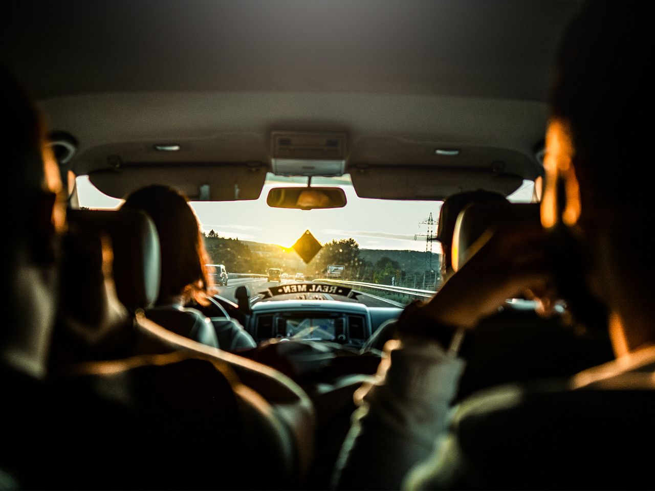Interior view of a car during a sunset road trip with passengers enjoying the drive.