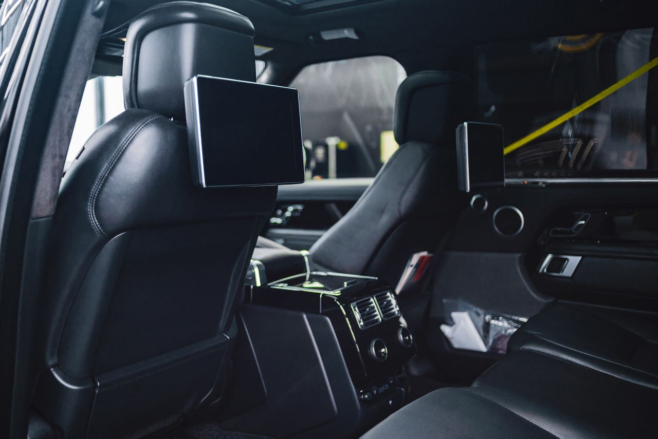 Contemporary style auto interior with rectangular displays on back seats and entertainment equipment with buttons in daylight